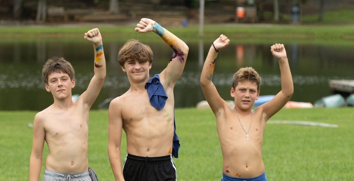 Image shows 3 young men raising their arms in victory after winning a game.