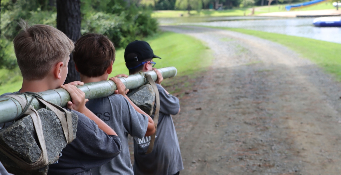 Image shows students carrying a rock tied to a bamboo poll.